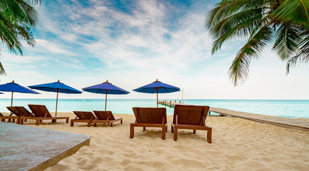Wooden beach chair and beach umbrella at sand beach of resort beside the bridge. Summer vacation travel. Tropical holiday travel. Three couple sunbed and coconut tree with blue sky and white clouds.