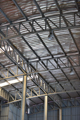An interior space of a factory shop showing a scaffolding metal roof sheet with a framework of metal truss with sunlight goes through.