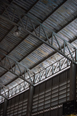 An interior space of a factory shop showing a scaffolding metal roof sheet with a framework of metal truss with sunlight goes through.