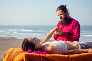 Fototapeta na wymiar Therapeutic massage on the shore of the tropical sea. Ayurvedic relaxing massage woman in spa salon getting massage on the holiday beach.girl lying down on the table treatment procedure