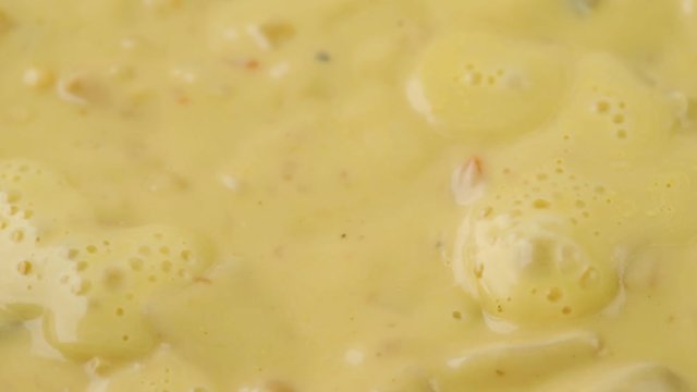 Very close video of chicken corn chowder starting to boil while cooking illuminated with natural lighting.