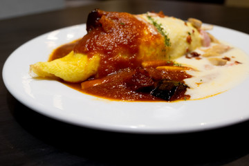 An omelet with rice in tomatoes sauce with grilled eggplant and mushroom cream sauce.