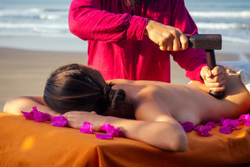 male master makes Thai massage Tok-sen spa therapy physiology by the sea ocean beach.Beautiful woman having a relaxing thai back massage with set for massage toksen,Body care relaxation resort © yurakrasil
