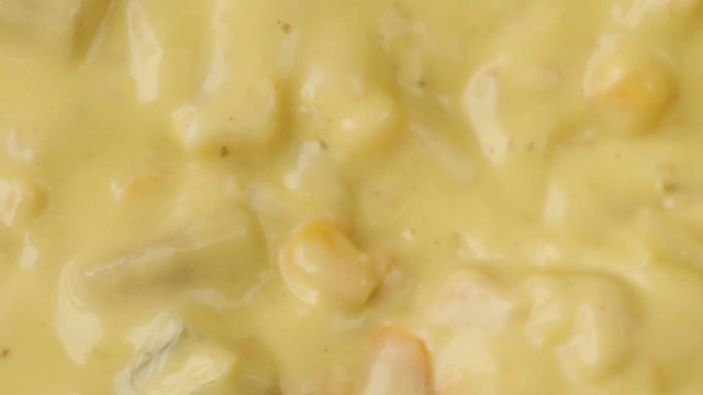 Very close video of stirring and taking a spoonful of chicken corn chowder illuminated with natural lighting.