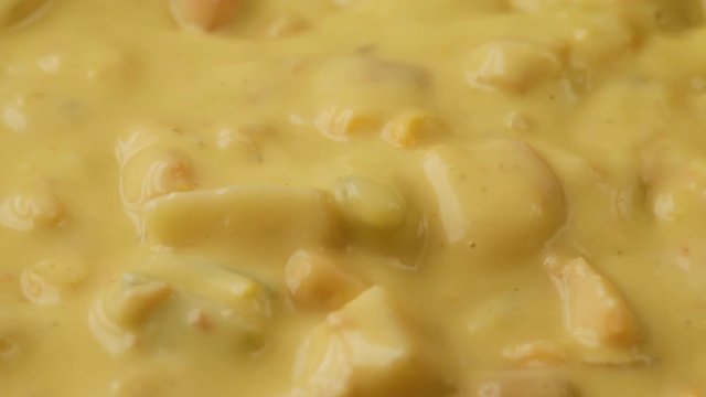 Very close video of stirring and taking a spoonful of chicken corn chowder illuminated with natural lighting.