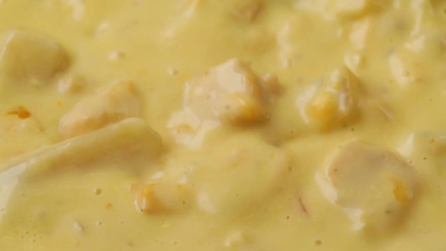 Close video of stirring hot chicken corn chowder and cheddar cheese with a spoon then taking a spoonful at the end illuminated with natural lighting.