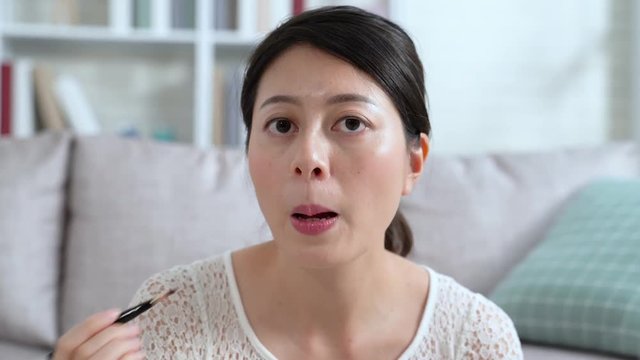 Makeup artist applies red pink lipstick. Beautiful woman face painting lips by brush. Make up in process young girl blogger looking camera satisfied with cosmetic smiling at home indoors.