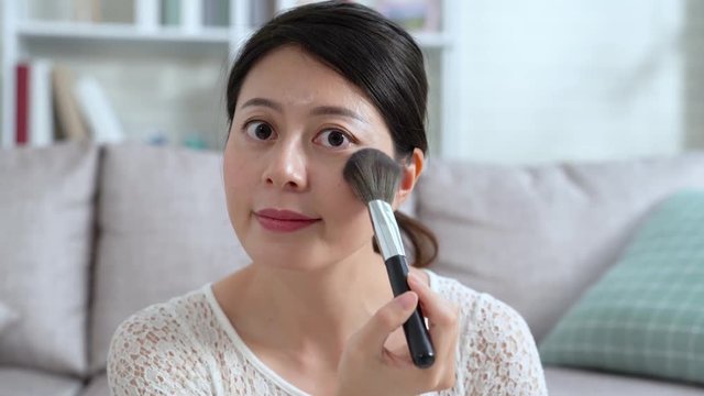 beautiful asian woman applying dry cosmetic tonal foundation on face using makeup brush looking camera recording video blog. online live streaming young people lifestyle concept. girl vlogger smiling
