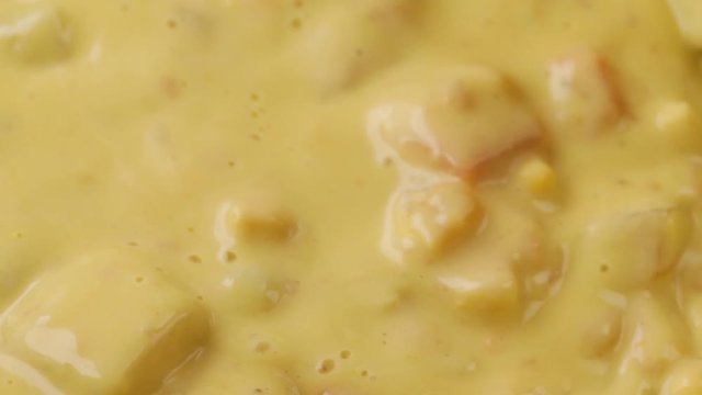 Close video of stirring hot chicken corn chowder with a wood spoon while heating illuminated with natural lighting.