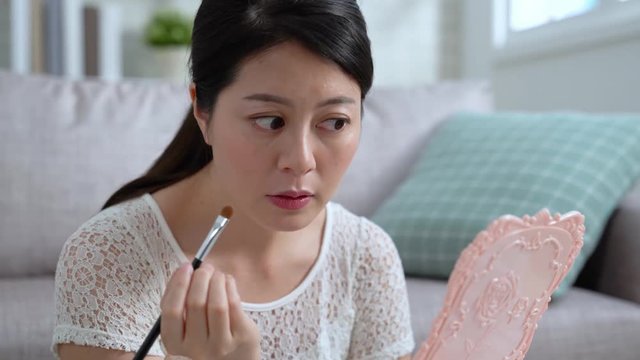 fast motion of happy young beauty girl makeup at home in morning get ready. beautiful asian woman using brush applying eyebrows looking at mirror sitting in apartment indoors. chinese lady prepared