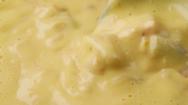 Close video of stirring hot chicken corn chowder with a spoon and taking a spoonful at the end illuminated with natural lighting.