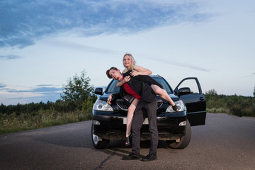 Naklejka premium Guy carrying the girl on the road near the car in a summer evening