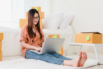 Freelancer woman working sme business at office in home interior smile checking order from laptop computer for customer and online delivery box for ready packing in bedroom.