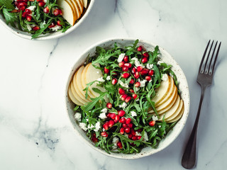 Vegan salad bowl with arugula, pear, pomegranate, coconut crumble or cottage cheese on marble...