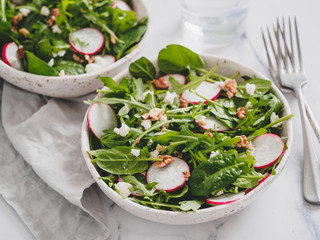 Vegan salad bowl with arugula, spinach, radish, coconut crumble or cottage cheese, walnut. Vegan breakfast, vegetarian food, diet concept. Two bowls with salad on white marble tabletop