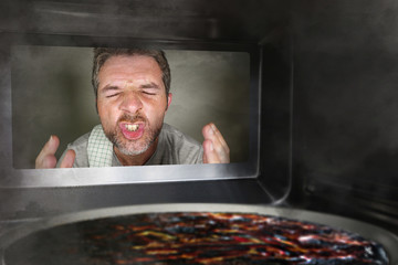 messy and funny dummy man in the kitchen looking through microwave or oven pizza burning overcooked...