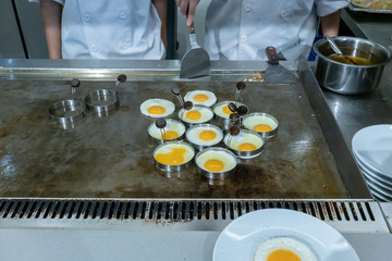 Hotel chef hands with gloves cooking fried eggs  on hot pan