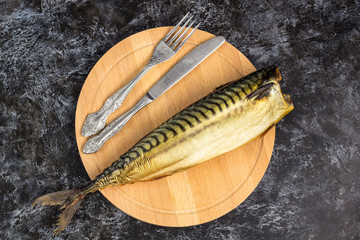 Smoked mackerel without head with fork knife cutting board on black background