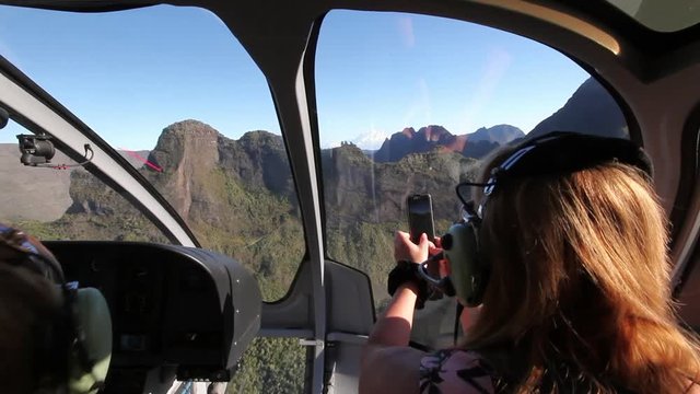 Woman near boy shoots video on smartphone from cockpit in helicopter.