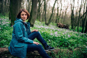 Obraz premium Toned photo of happy hiking middle-aged woman in blue jacket sitting and resting in evening spring forest