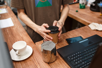 Barista pours coffee into a disposable paper cup. 