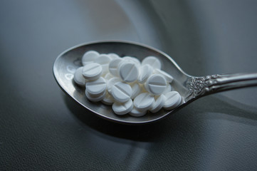 Lot of white pills in a spoon on a gray dark background. Overdose medication.