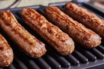 Serbian cevapi, cevapcici, Balkan minced meat kebab. Sausages cooking to grill. Close-up