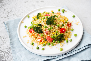 Lenten dish. Bulgur with vegetables in a plate. Pilaf from bulgur, broccoli, green peas, bell peppers and corn.