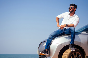 Successful young businessman sunglasses on a beach. Afro man leaning on his car parked in front of ocean on road trip enjoying peace and silence relaxing on nature.Summer vacations and travel concept