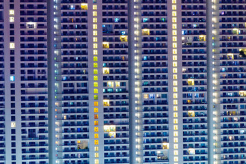 Fototapeta na wymiar Tall residential highrise with apartment windows lit at night. Individuality in big city living. Condos for sale and rent.