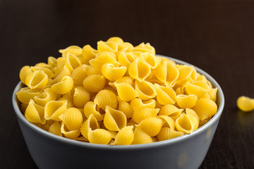 black background with italian raw conchiglie paste shells in bowl with copy space