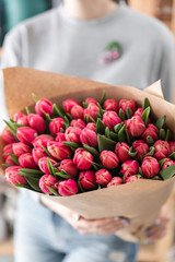 Young beautiful woman holding a spring bouquet of red tulips in her hand. Bunch of fresh cut spring flowers in female hands