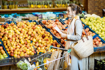 Young woman holding meal plan while buying healthy food in the supermarket with apples on the background