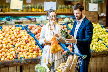 Young and happy couple buying fresh fruits and vegetables standing together with shopping cart in the supermarket