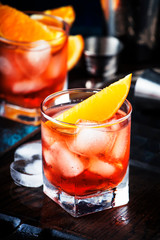 Summer alcoholic cocktail Negroni with dry gin, red vermouth and red bitter, orange slice and ice cubes. Brown bar counter background, bar tools, place for text, selective focus