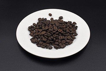 Coffee beans scattered on a white plate with a black background