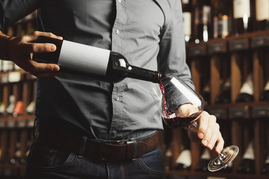 Close up photo of male sommelier pouring red wine into wineglasses. Waiter with bottle of alcohol beverage.