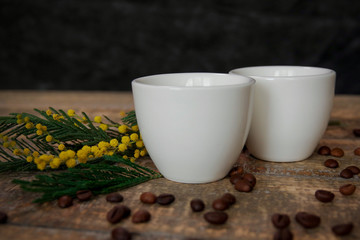 Coffee cups with coffee beans and a sprig of mimosa