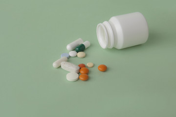 Pills, tablets and capsules and a bottle on a green background. Copy space for text.