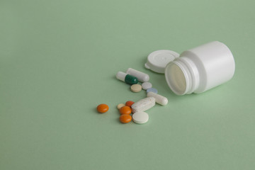 Pills, tablets and capsules and a bottle on a green background. Copy space for text.