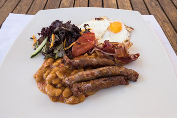 English breakfast. Breakfast served on a wooden table with sausages, eggs, bacon, beans, toast.