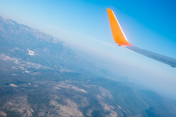 Fototapeta na wymiar Airplane wings in the blue sky and a mountains view scene. Travel and adventure.