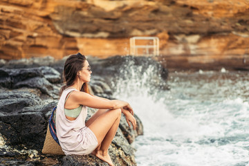 Pretty long hair brunette tourist girl relaxing on the stones near sea.