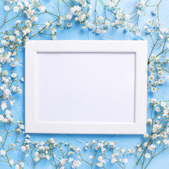 Empty  white frame and  fresh white gypsofila  flowers on blue textured background.