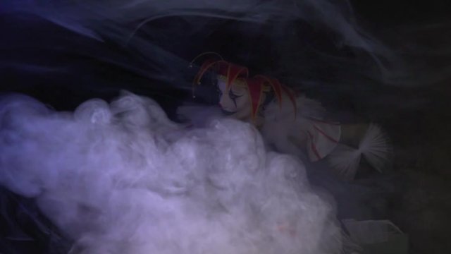 Female jester with a red hat on her head and amazing makeup is sitting in the smoke, slow motion