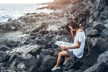 Pretty long hair tourist girl relaxing on the stones near sea.