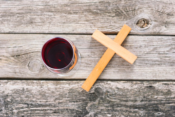 wooden cross and glass of red wine on old wood table