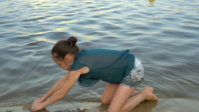 A little girl plays on the beach at sunset and builds a tower of sand on the background of calm water. Portrait. Close up. 4k. 25 fps.