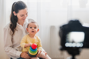 Fototapeta premium Beautiful baby toddler with young mother in front of the camera vlogging or blogging indoors