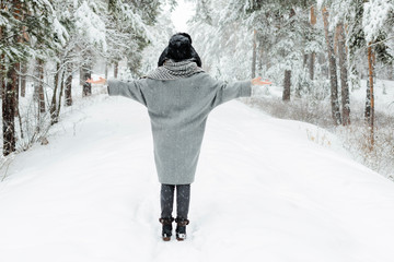 Beautiful young woman standing among snowy trees in winter forest and enjoying snow.